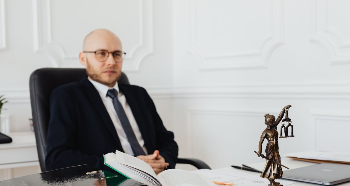 Avocat la birou, cu statueta justitiei si dosare, lucrand cauze din oficiu